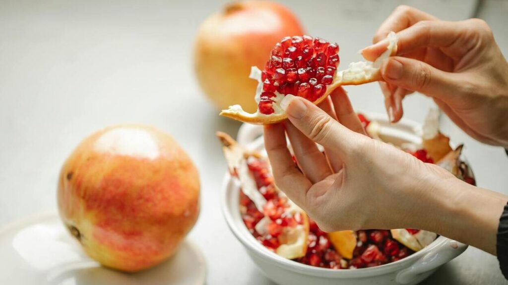 ALT OPIS (SEO + dostępność)Dłonie kobiety rozłupujące owoc granatu — naturalne źródło błonnika wspierającego zdrowie jelit i mikrobiotę jelitową.