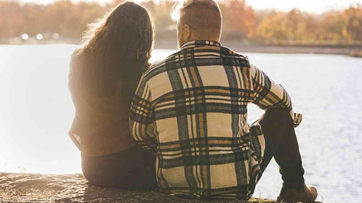 Para siedzi obok siebie nad jeziorem, patrząc w dal bez kontaktu wzrokowego, co pokazuje, jak satysfakcja w relacji może słabnąć mimo bliskości.