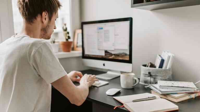 mężczyzna w białej koszulce klika w komputer przy biurku
