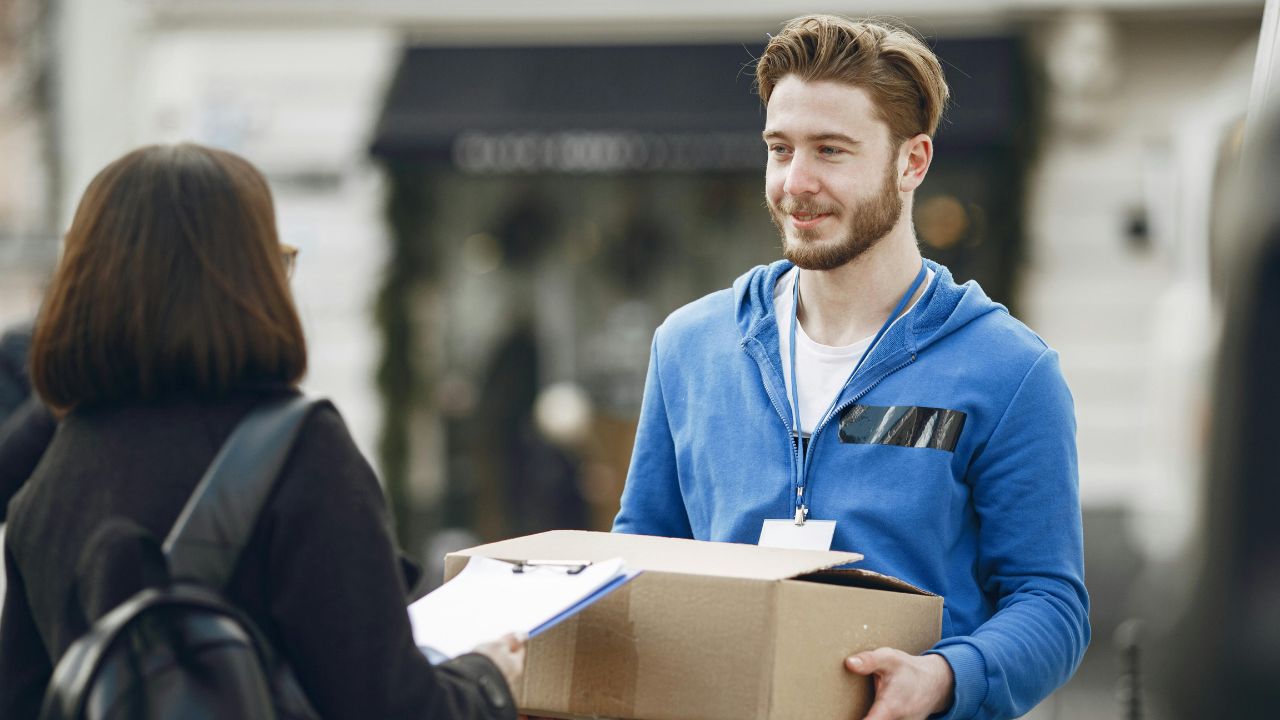 mężczyzna w niebieskiej bluzie przekazuje paczkę kobiecie