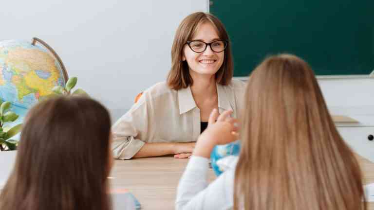 nauczycielka siedzi za biurkiem i patrzy na uczniów. Jak będzie wyglądała szkoła po zmianach MEN w edukacji?