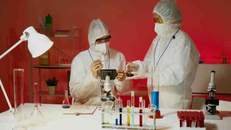 Dwóch naukowców w ochronnych kombinezonach pracuje przy mikroskopie w nowoczesnym laboratorium genetycznym, analizując próbki i dane DNA na stanowisku badawczym.