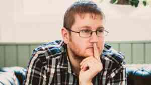 Mężczyzna w okularach siedzi zamyślony, podpierając twarz dłonią – ilustracja tematu kłopotów z pamięcią i koncentracją.