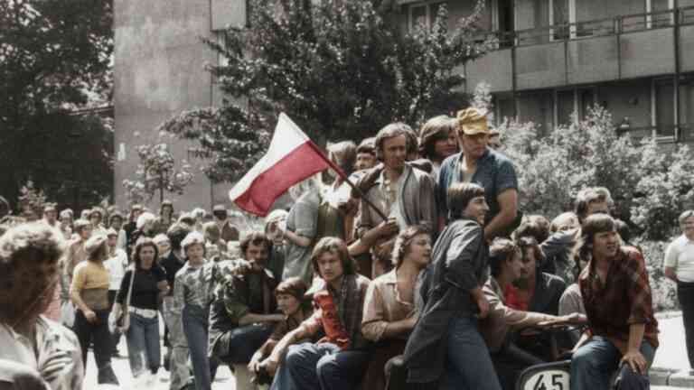Tłum ludzi siedzących na ciężarówce podczas protestu w PRL; młodzi robotnicy i mieszkańcy trzymają biało-czerwoną flagę w czerwcu 1976 roku w Radomiu.