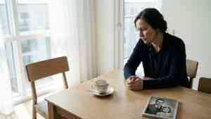 Smutna kobieta siedząca przy stole naprzeciwko pustego krzesła, co obrazuje psychologiczne skutki braku ojca.