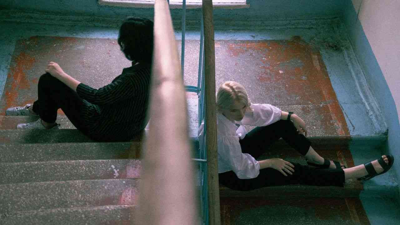 Dwie osoby siedzą na schodach tyłem do siebie. Zdjęcie ilustruje wpływ miejsca zamieszkania i konfliktów sąsiedzkich na długość życia.