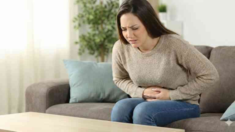 Młoda kobieta z wyrazem bólu na twarzy trzyma się za brzuch, ilustrując potrzebę powiedzenia stop stanom zapalnym.