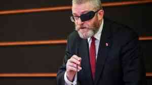 Grzegorz Braun w garniturze i opasce na oku mówi do mikrofonu