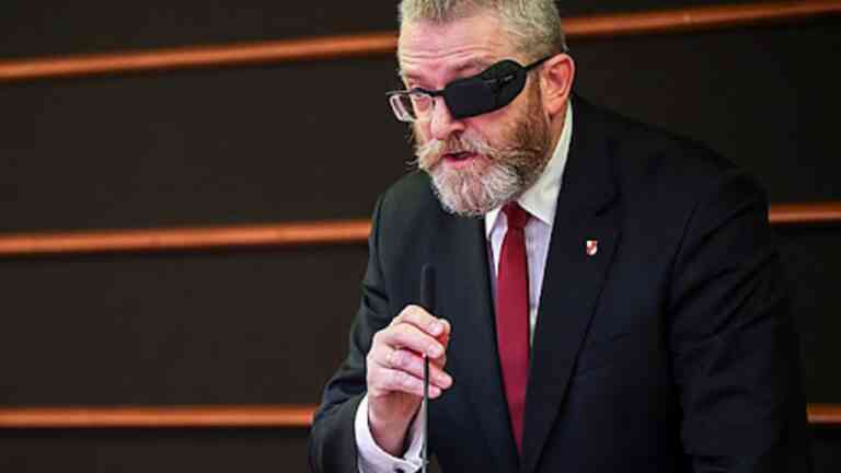Grzegorz Braun w garniturze i opasce na oku mówi do mikrofonu