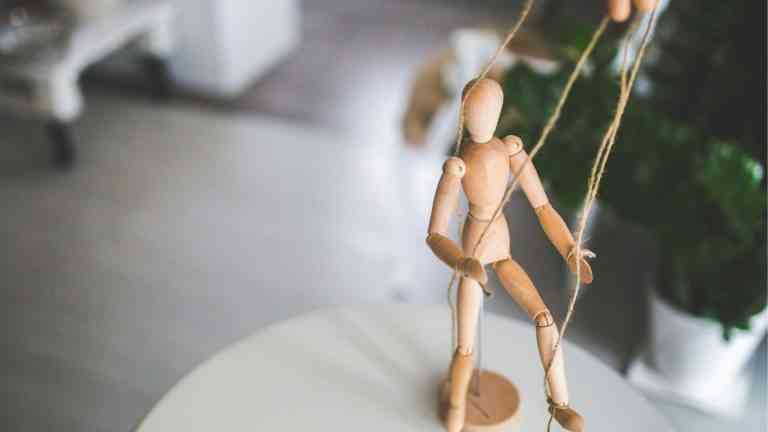 drewniany ludzik w kształcie marionetki trzymany przez człowieka symbolizuje algorytmy mediów społecznościowych