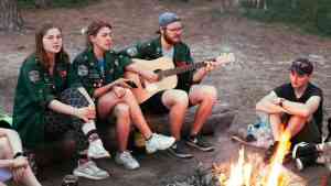 Grupa ludzi gra i śpiewa przy ognisku. Tekst stara się odpowiedzieć na pytanie czym jest przyjaźń.