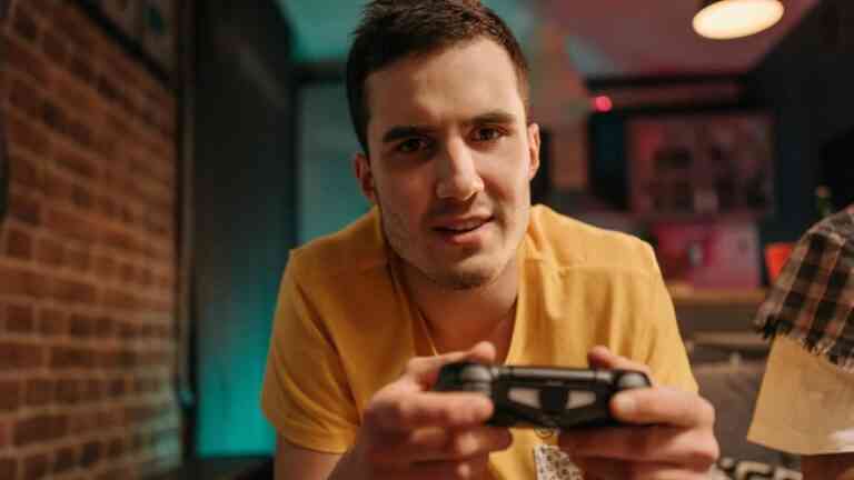 Młody mężczyzna trzyma kontroler i gra na konsoli w domowym wnętrzu – temat artykułu o tym, jak gry wideo demencja mogą być powiązane z profilaktyką chorób neurodegeneracyjnych.