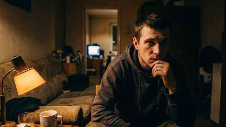 Nocny tryb życia a charakter - zamyślony młody mężczyzna siedzi w ciemnym, nastrojowym salonie, oświetlony lampą stołową, trzymając rękę przy brodzie.