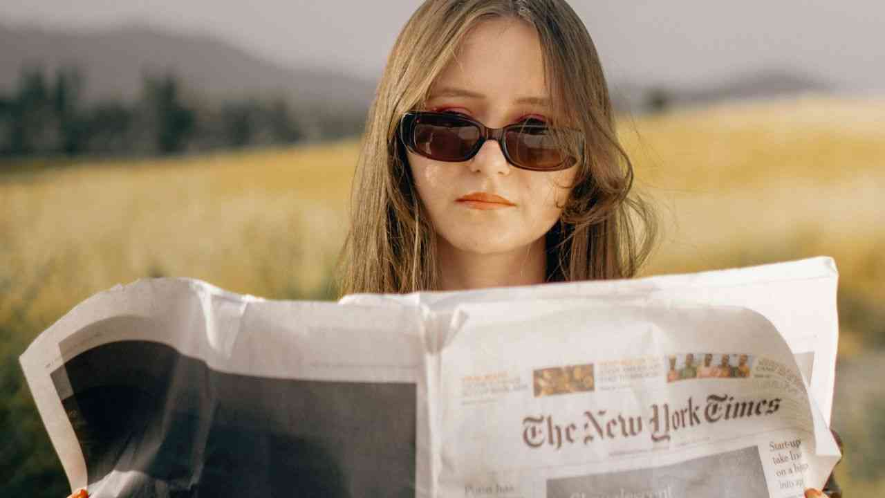 kobieta czyta gazetę w okularach za nią łąka