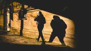 Mężczyzna w kapturze idzie drogą, za nim jest cień