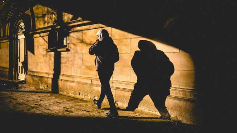 Mężczyzna w kapturze idzie drogą, za nim jest cień
