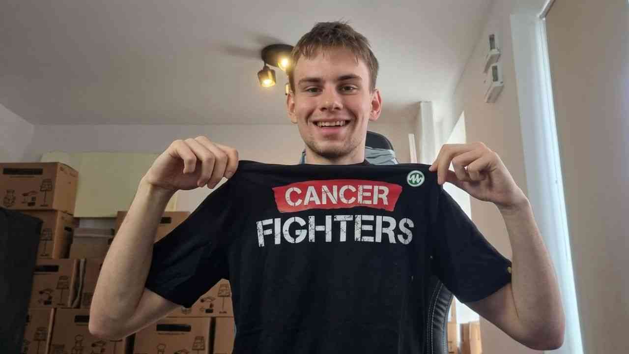 uśmiechnięty chłopak Łatwogang trzyma czarną koszulkę z białą nazwą Cancer Fighters