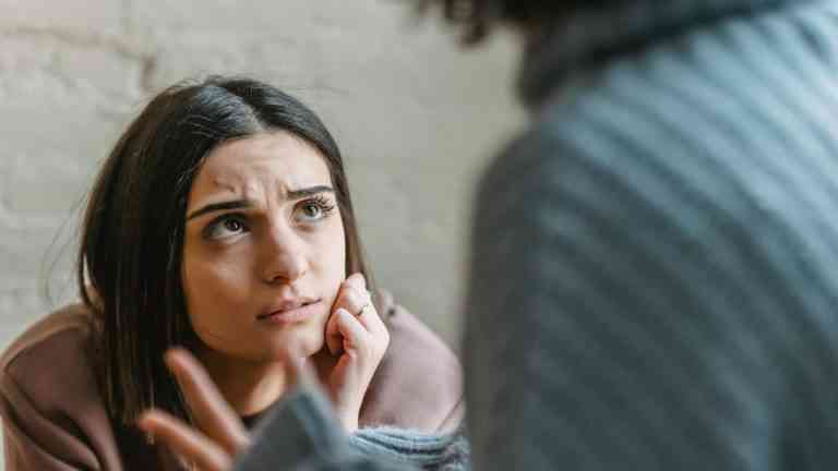 Kobieta słucha w napięciu podczas trudnej rozmowy, emocje po zranieniu w relacji