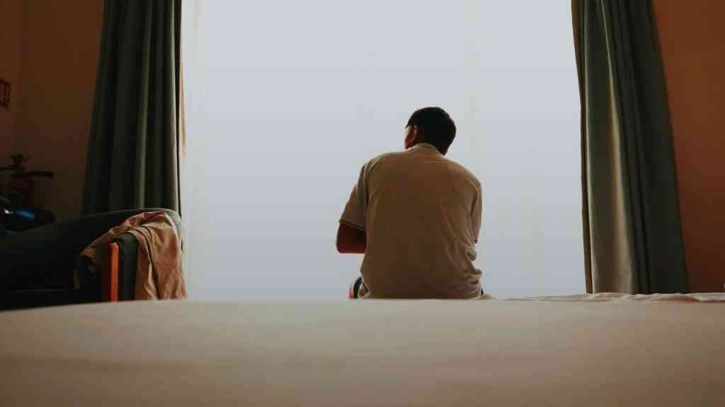 Mężczyzna siedzący samotnie przy oknie w półmroku, symbol refleksji nad tym, dlaczego czujemy ból i jaki jest sens ludzkiego bólu