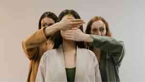 trzy kobiety, dwie z nich zasłaniają twarz trzeciej