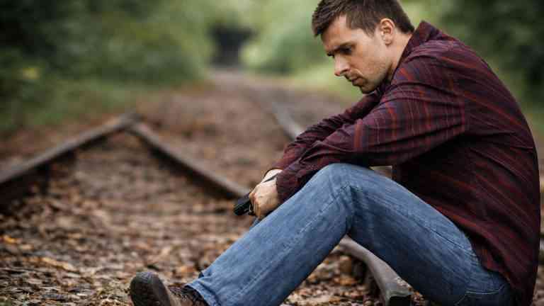 Mężczyzna siedzący przy torach kolejowych, zamyślony, symboliczny moment refleksji i próby rozpoczęcia życia od nowa