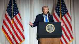 Donald Trump przemawia przy prezydenckiej mównicy na tle amerykańskich flag. Zdjęcie ilustruje tekst o drugiej kadencji Trumpa, wojnie z Iranem i sporze wokół jego politycznych obietnic.