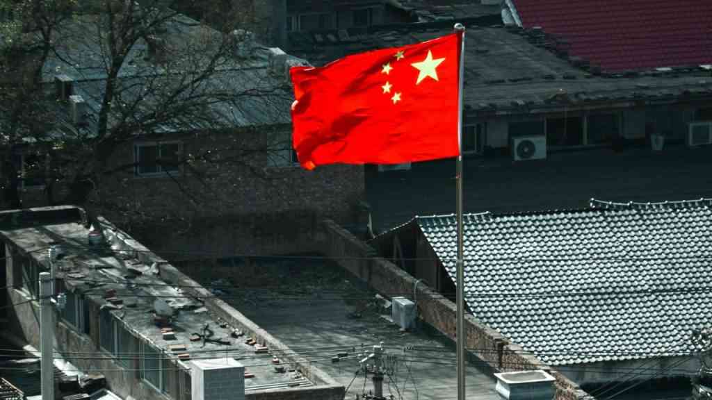 zbliżenie na flagę Chin powiewającą na wietrze, na tle stare szare budynki. Tam rodzi się nowe Imperium Zła