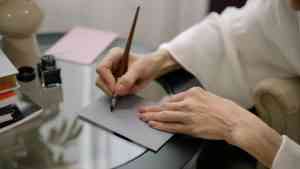 Kobieta pisze list pisany odręcznie piórem na kartce przy biurku