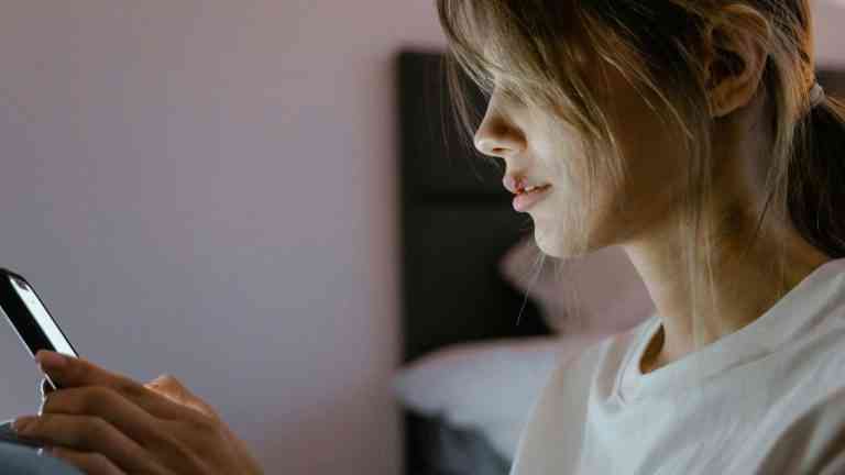 młoda kobieta w białej bluzce przegląda media społecznościowe w samotności