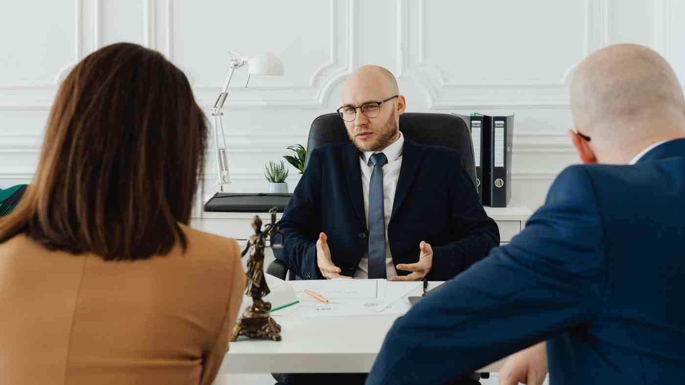 Prawnik siedzący za biurkiem i rozmawiający z klientami, którzy mają swoje opinie o prawnikach