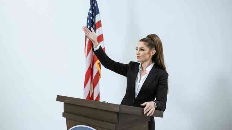 Kobieta w czarnej marynarce stojąca za podium. Polityka wydłużania życia na świecie ma różne oblicza.