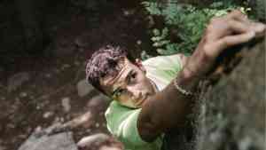 młody mężczyzna wspina się po skałach w jasnej koszulce, pokazuje czym jest pokonywanie ograniczeń życiowych