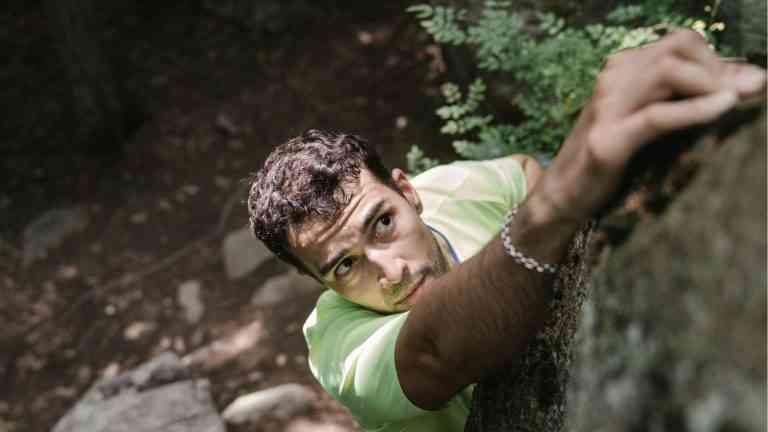 młody mężczyzna wspina się po skałach w jasnej koszulce, pokazuje czym jest pokonywanie ograniczeń życiowych