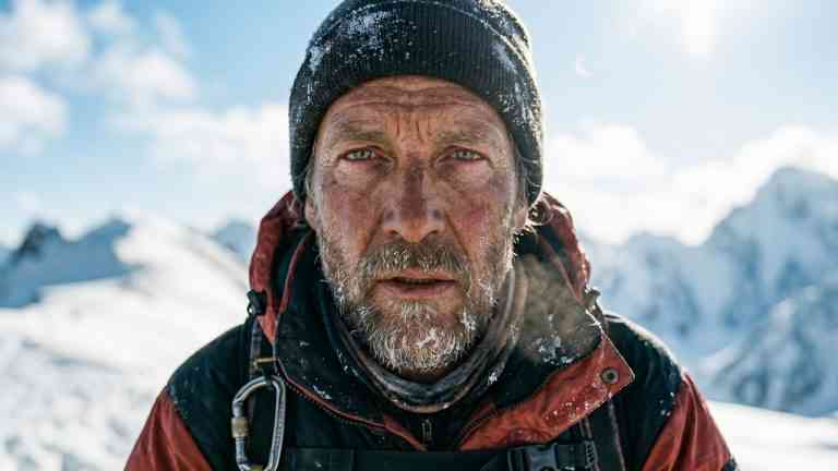 Portret zmęczonego wspinacza z oszronioną brodą na tle ośnieżonych szczytów – temat: polscy himalaiści i ich rodzina.