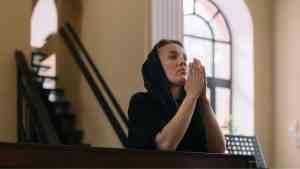 Kobieta ubrana na czarno modli się w kościele, życie po porzuceniu wiary