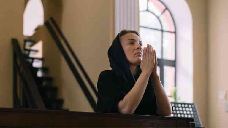 Kobieta ubrana na czarno modli się w kościele, życie po porzuceniu wiary
