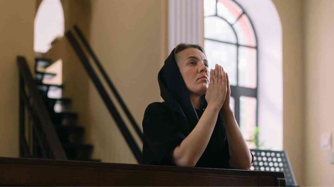 Kobieta ubrana na czarno modli się w kościele, życie po porzuceniu wiary