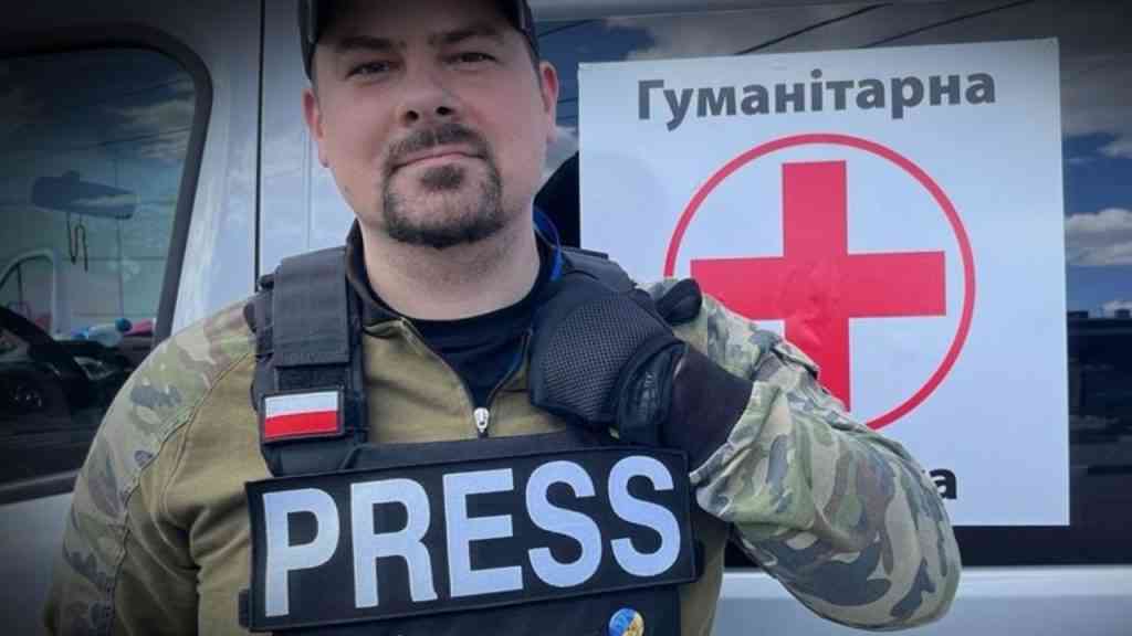 Michał Bruszewski pozuje na tle ukraińskiego samochodu w kamizelce kuloodpornej.