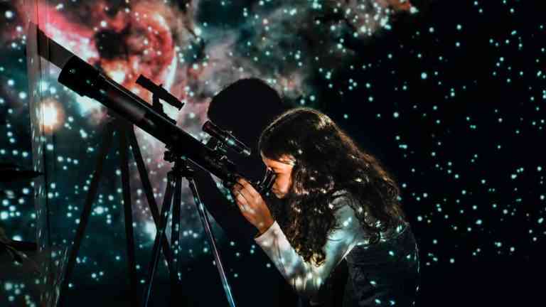 Dziewczynka spoglądająca w teleskop w stronę nocnego nieba, ilustrująca jak astronomia w szkole rozpala w dzieciach ciekawość świata.