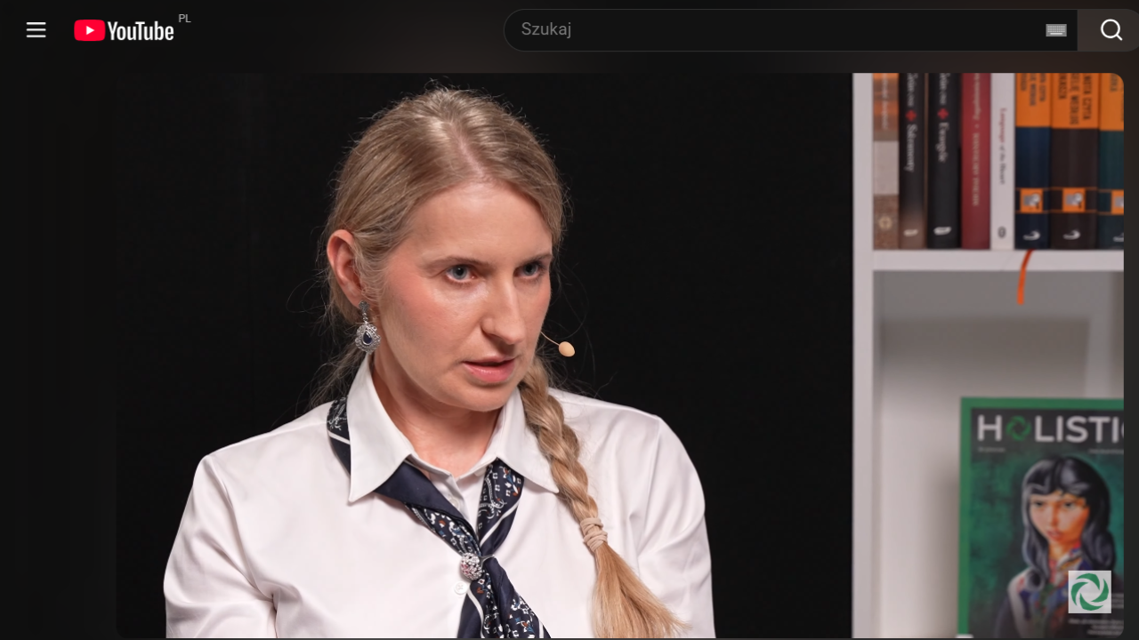 Anna Zapolska, ekspertka od survivalu miejskiego, w białej koszuli z ciemną apaszką, podczas wywiadu w studiu Holistic News. W tle widoczny regał z książkami i logotyp portalu.