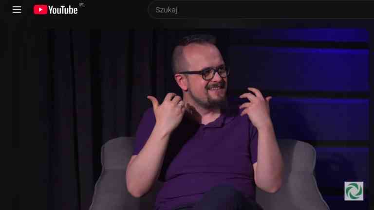 Uśmiechnięty Szymon Pękala w studiu Holistic News gestykuluje, tłumacząc jak przekonać kogoś o odmiennym światopoglądzie.