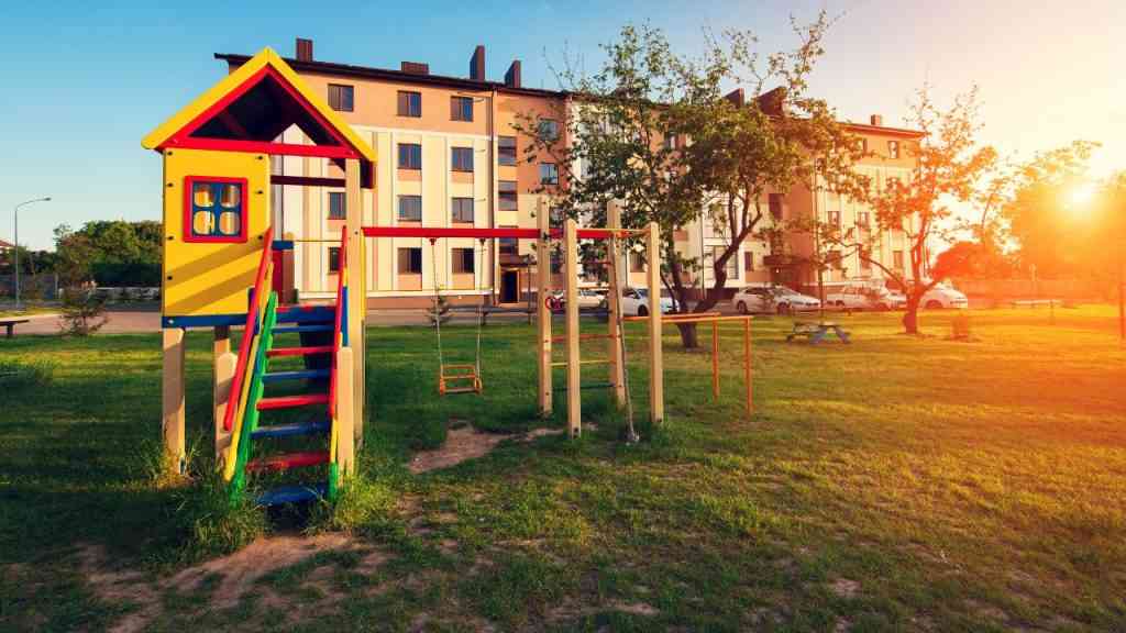 Pusty plac zabaw dla dzieci a obok blok mieszkalny. Ilustruje problem uzależnienia dzieci od telefonu.