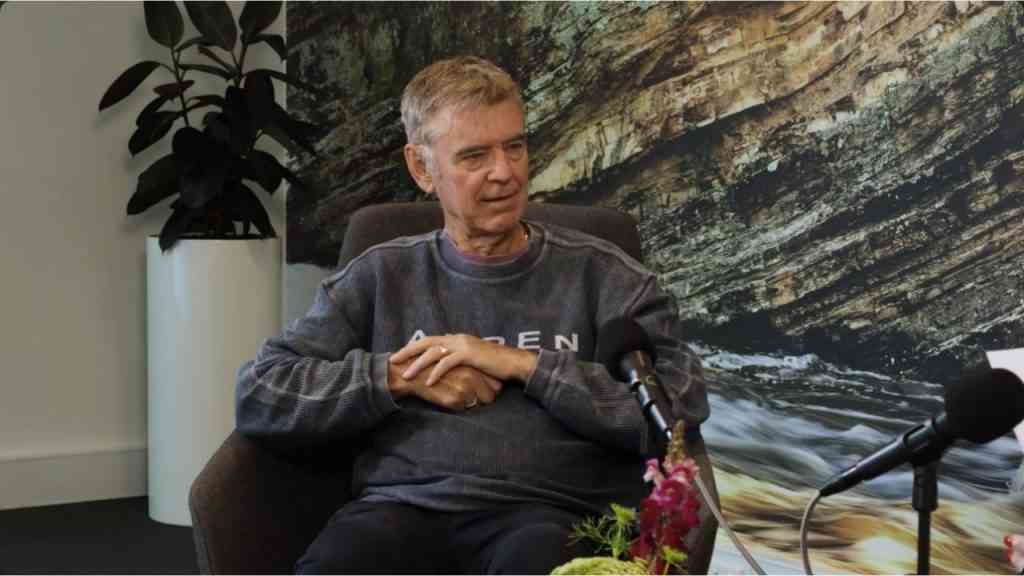 John Hattie siedzi w fotelu w ciemnych ubraniach i opowiada, jak rozpoznać dobrą szkołę