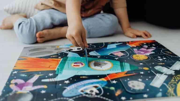Dziecko rozwiązujące kolorowy puzzle o tematyce kosmicznej na podłodze, zajęcie edukacyjne ilustrujące naukę przez zabawę