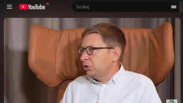 Michał Bilewicz, psycholog społeczny, w okularach i jasnej koszuli, siedzi w brązowym skórzanym fotelu uszaku i z zaangażowaniem wypowiada się podczas wywiadu wideo.