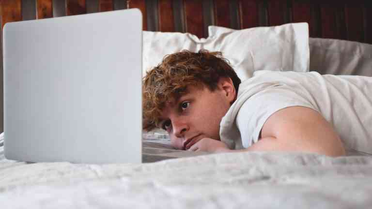 nastolatek leży na łóżku, patrząc w laptopa, co pokazuje nadmierne korzystanie z internetu