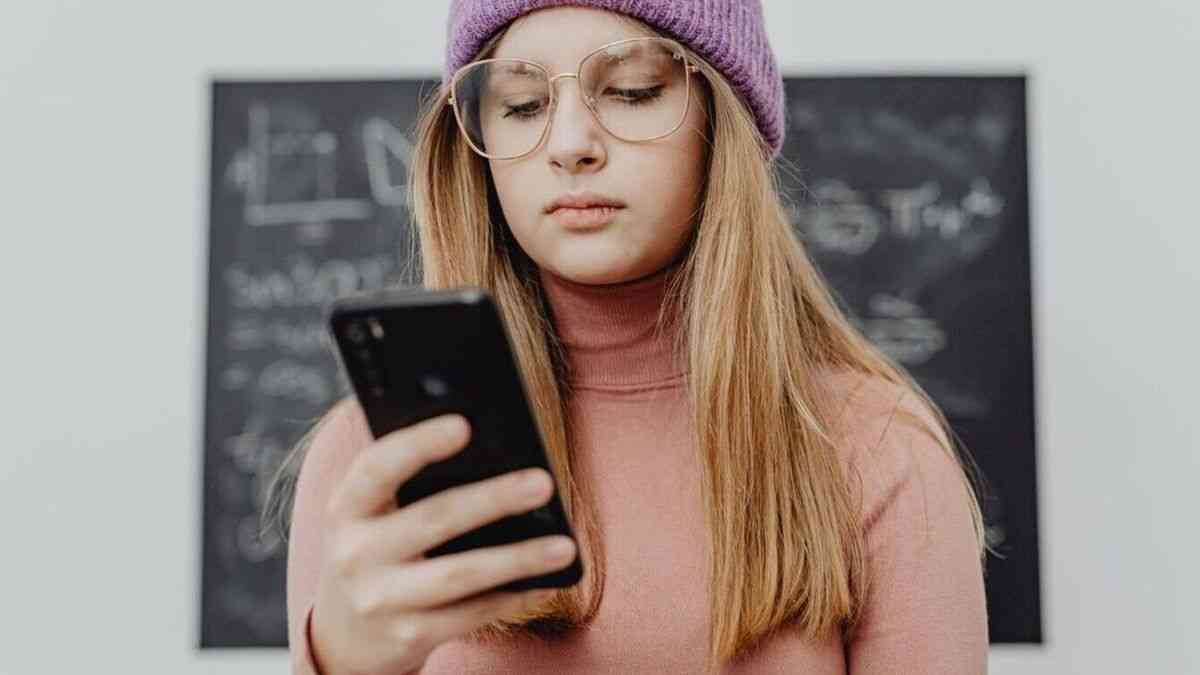 Nastolatka ze smartfonem an tle szkolnej tablicy obrazująca wpływ uzależnienia od TikToka na naukę