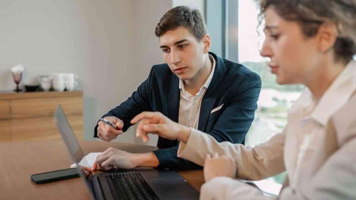 Dwoje pracowników rozmawia przy laptopie o AI w pracy