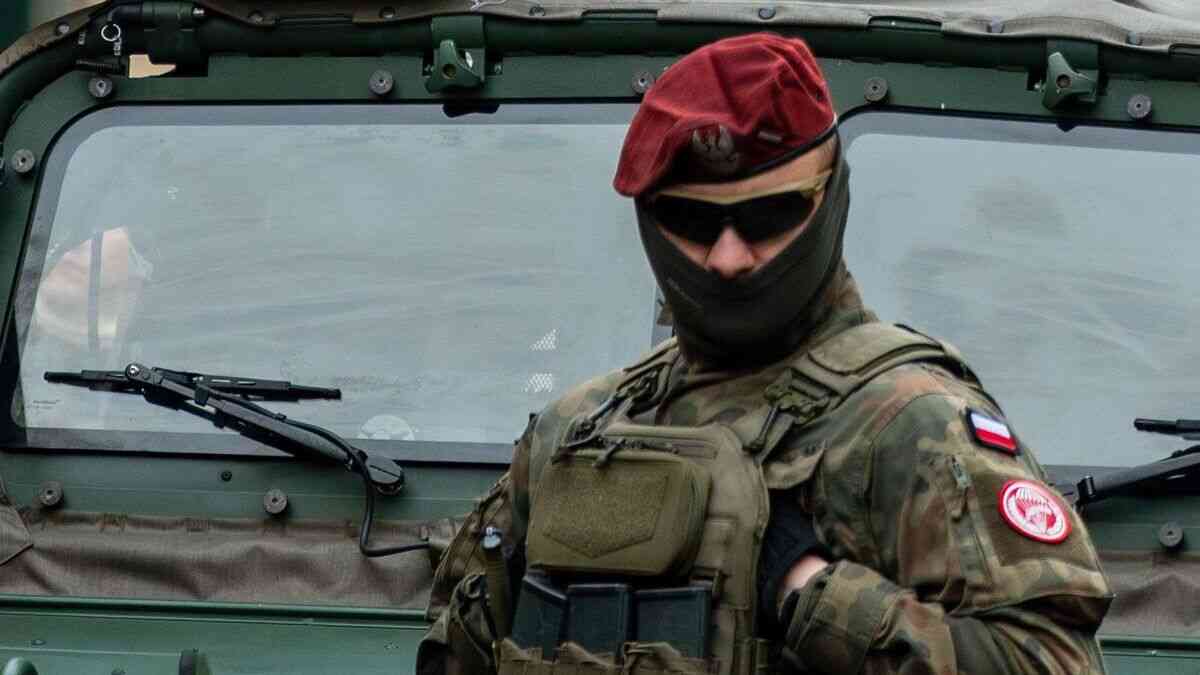 Polski żołnierz w mundurze stoi przed pojazdem wojskowym, symbolizując przygotowanie na wojnę